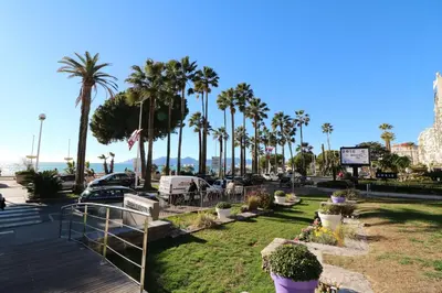 a park with palm trees and chairs and a boardwalk at Beautiful studio at the Grand Hotel Residence with sunny balcony 138 in Cannes