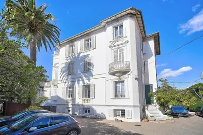 a white building with a palm tree in front of it at IMMOGROOM - Bourgeois building - Quiet - Parking - Sea view in Cannes