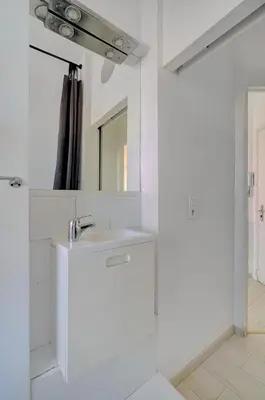 a white bathroom with a sink and a mirror at IMMOGROOM - Bourgeois building - Quiet - Parking - Sea view in Cannes