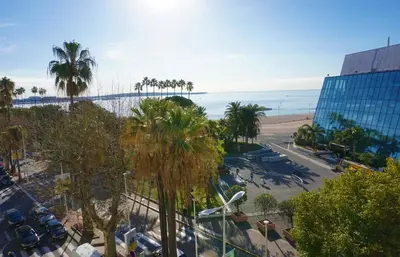 a view of a beach with palm trees and a building at LEM5D - Palmes d'Or Properties in Cannes