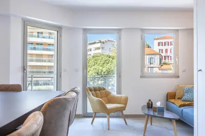 a living room with a table and chairs and windows at LB Vacation Rentals I Cannes Center, Renovated Apartment with Balcony, Ideal for Holidays or Congress! in Cannes