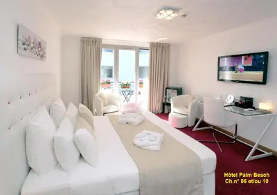 a white bedroom with a large white bed and a desk at HOTEL PALM BEACH in Cannes