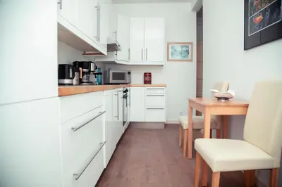 a kitchen with white cabinets and a wooden table at AnaZa Appartement in Cannes