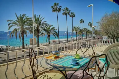 a table and chairs next to a beach with palm trees at 2 pièces TERRASSE vue MER- 20 m de la PLAGE A1B120 in Cannes