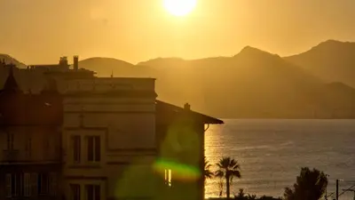 a sunset over the water with a building and mountains at 3 StarsStudio54 23 Ave Laugier100m Plages Mistral in Cannes