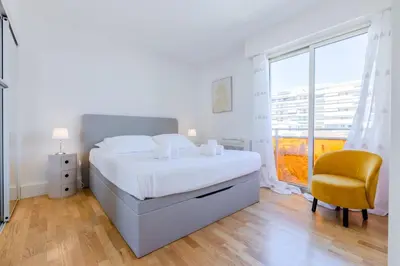 a white bedroom with a bed and a yellow chair at Stylish 1-Bedroom Apartment Close to Beaches in Cannes