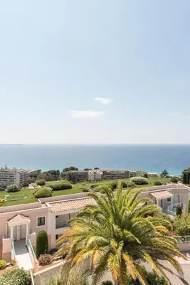 a palm tree in front of a building and the ocean at Résidence Cannes Villa Francia - maeva Home - Appartement 2 pièces 4 personnes - Budget MAE-8884 in Cannes