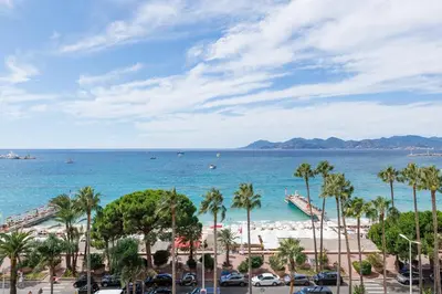 a view of a beach with palm trees and the ocean at Palais des Iles YourHostHelper in Cannes