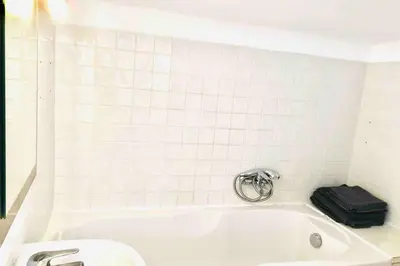 a white tiled bathroom with a bath tub with a suitcase at MIPIM Rue Montaigne, 200m Palais des festivals in Cannes