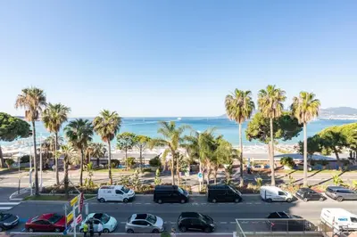a parking lot with cars and palm trees and the ocean at REF 1426 - Cannes Croisette - Sea view apartment for rent in Cannes