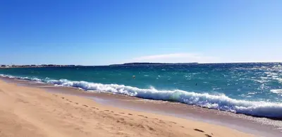 a sandy beach with a wave in the ocean at Appartement charmant à Cannes avec vue sur la mer, 33 m² in Cannes
