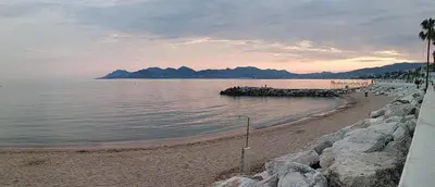 a beach with rocks and the ocean with mountains in the background at Beau meublé 3 pièces 60 m² Cannes Le Suquet in Cannes