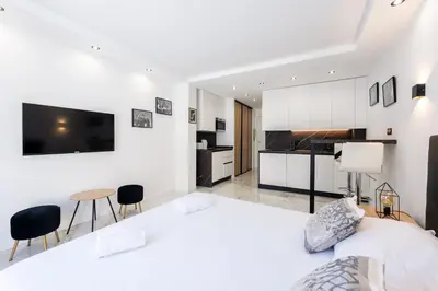 a white bedroom with a large bed and a kitchen at Large studio - 50m Cannes beach - terrace sea view in Cannes