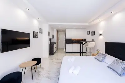 a white bedroom with a large bed and a kitchen at Large studio - 50m Cannes beach - terrace sea view in Cannes