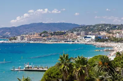 a view of a beach with palm trees and a city at On la Croisette XXL 1 bedroom with amazing sea view in Cannes