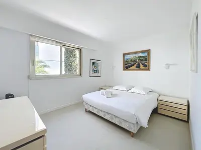 a white bedroom with a bed and a window at 2 bedroom apartment with parking 3 mins from La Croisette beach in Cannes