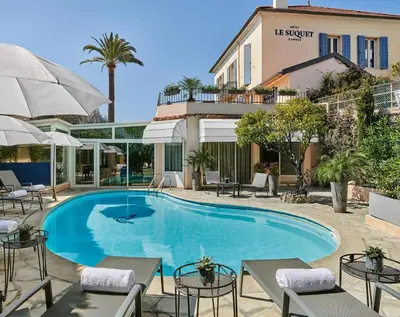 a swimming pool in front of a hotel with tables and umbrellas at Hotel Le Suquet Cannes in Cannes