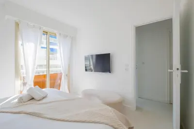 a white bedroom with a bed and a tv at Stylish 2-Br Apartment Steps from the Croisette in Cannes