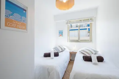 two beds in a room with white walls and a window at Stylish 2-Br Apartment Steps from the Croisette in Cannes