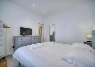 a white bedroom with a large bed and a television at LOENA CANNES CENTRE - 2 pièces rénové - 4 personnes - proche croisette palais festival plage - internet gratuit - climatisation - non fumeur in Cannes