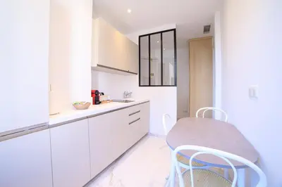 a white kitchen with white cabinets and a stool at L'Elégance Hoche - Congrès Palais - Plage Croisette - Cannes Centre - Clim in Cannes