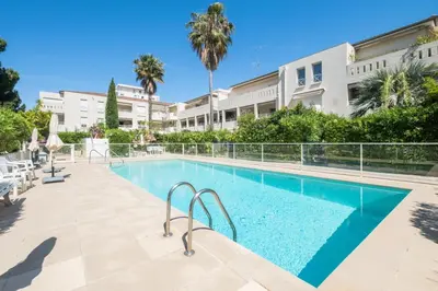 a swimming pool in front of a building with palm trees at Comfy apartment with residential swimming pool in Cannes