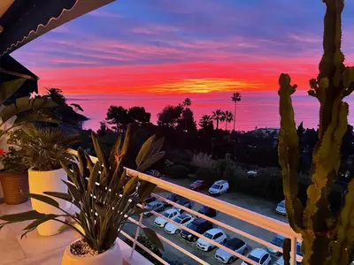 a sunset from a balcony with cars parked in a parking lot at Royal Pink - Appartement design - Vue de rêve - Parking gratuit in Cannes