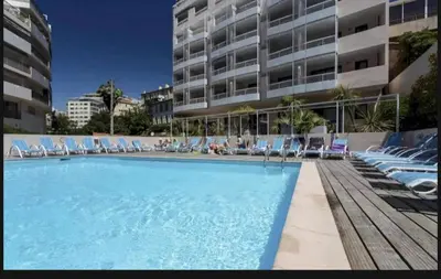 a large swimming pool with chairs and a building at Azur Éden Studio avec Piscine à Deux Pas de la Plage in Cannes
