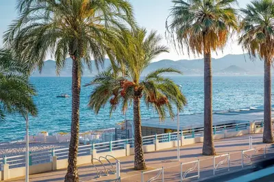 a row of palm trees next to the ocean at Bel Appartement Face à La Mer Près Du Centre - Le Voilier by Halldis in Cannes