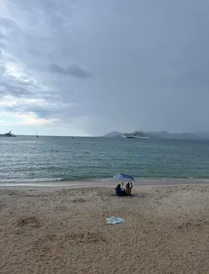 two people sitting under an umbrella on the beach at Croisette Beach & Palace in Cannes