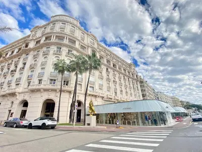 a large white building with palm trees in front of it at Croisette Beach & Palace in Cannes