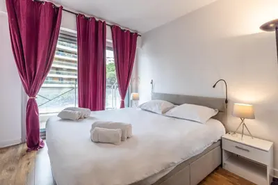 a bedroom with a large white bed with purple curtains at LB Vacation Rentals I High Floor Sea View 2Br Apt with Balcony & Garage in Cannes