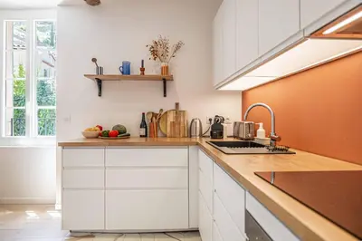 a kitchen with white cabinets and an orange wall at L'EMERAUDE duplex confortable au cœur de Cannes, proche plage du Midi et Palais in Cannes