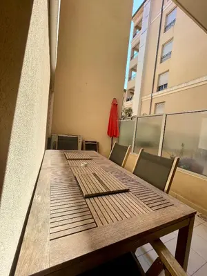 a wooden table on a balcony with chairs and a building at Jolie 3 pièces avec terrasse au vieux port, à 2 pas des plages et du palais. in Cannes