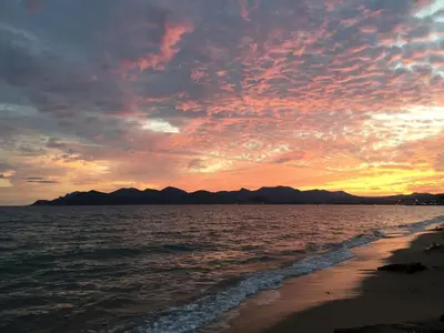 a sunset on the beach with mountains in the background at Océan front apartment in Cannes