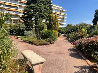 a park with a bench and flowers and a building at Parc De La Croisette in Cannes