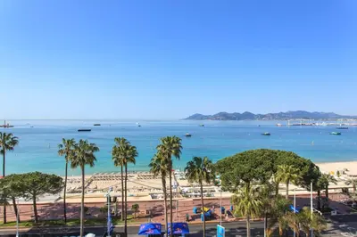 a view of a beach with palm trees and the ocean at REF 1196 - Cannes Croisette - Sea view apartment for rent in Cannes