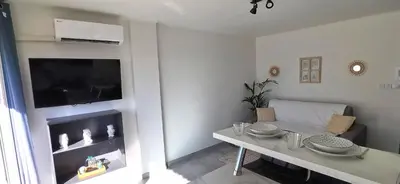a white living room with a table and a tv at Cannes Pointe Croisette studio plage 2 min à Pieds in Cannes