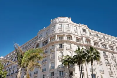 a large white building with palm trees in front of it at Palais Miramar - Suite Blue Room - Vue Mer -Croisette Emplacement Unique - 20M Plage - WIFI - Clim in Cannes