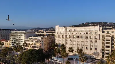 a bird flying over a large building with palm trees at CROISETTE VUE MER LATERALE in Cannes