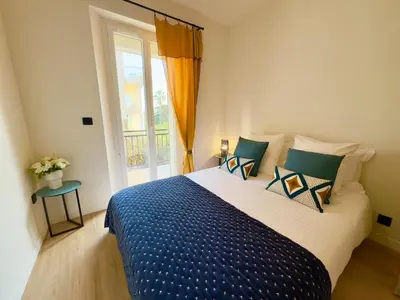 a bedroom with a bed with a blue comforter and a window at Luxueux 3 pièces - 2 chambres avec Terrasse, 4 mn Palais in Cannes