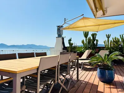 a wooden table and chairs on a deck with an umbrella at Superbe Penthouse avec vue panoramique sur la mer in Cannes