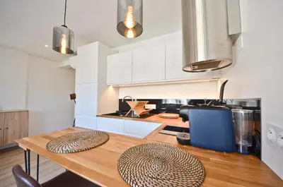 a kitchen with white cabinets and a wooden table at Le Flore - Appartement neuf - Cannes Center in Cannes