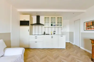 a kitchen with white cabinets and a white couch at L'ALIZEE avec jolie terrasse vue sur la ville, charmant studio dans le centre de Cannes in Cannes