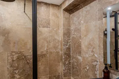 a shower in a bathroom with brown tiles at LE COCON- Jacuzzi & Sauna privés By SweetDreams in Le Cannet