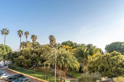 a parking lot with palm trees and parked cars at Le Mistral - Appt avec deux balcons à Cannes in Cannes