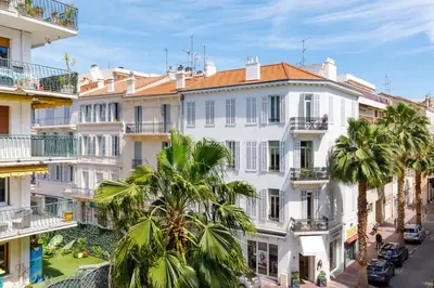 a white building with palm trees in front of it at Perle Dorée YourHostHelper in Cannes