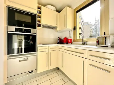 a kitchen with white cabinets and a large window at Cannes Center - Appartement 2 pièces avec terrasse in Cannes