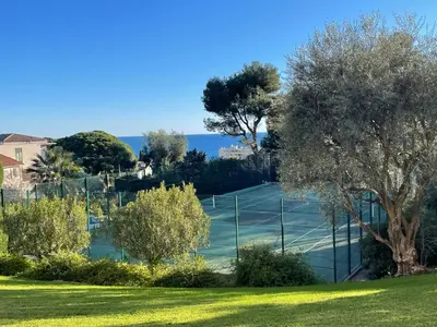 a tennis court with trees and the ocean in the background at C012-Appartement confortable avec piscine, tennis et grand parc in Cannes