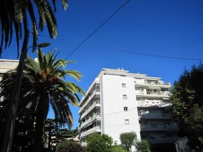 a tall white building with palm trees in front of it at Centre et plage tout à pied échappée mer in Cannes